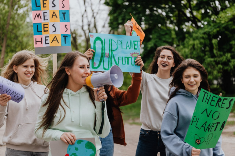 Group of young women at a climate protest holding signs with environmental messages outdoors.