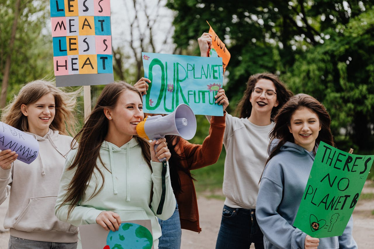 Group of young women at a climate protest holding signs with environmental messages outdoors.